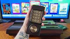 Hand holding Intellivision Sprint controller with console behind and TV displaying main menu in backdrop.