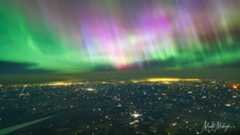 northern lights show in the sky, appears as curtains of purple and green light covering the entire sky. city lights are visible shining below.