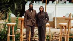 a man and a woman in brown standing in front of wicker stools in the sun