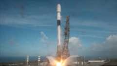A white and black rocket lifts off from its launch pad into a partially cloudy blue sky.