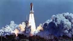 a white aircraft attached to a large orange rocket lifts off above a plume of fire and smoke