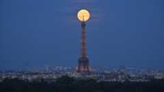 A bright full moon shines just behind the top of the Eiffel Tower in Paris.