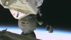 A small metal satellite is launched floating above Earth with part of the International Space Station seen on the left part of the image