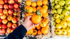 a hand holding an orange over baskets of fruit