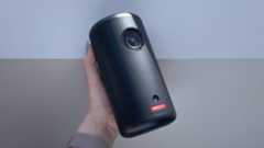 The Nebula Capsule 3 projector is being held to the light against a light grey background.