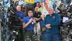 international space station astronauts cluster in a module. samantha cristoforetti is in front holding a microphone