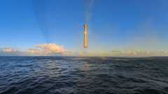 A giant metal cylinder hovers above a sea in front of a blue sky.