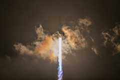 a white rocket lifts off at night above a plume of fire and smoke