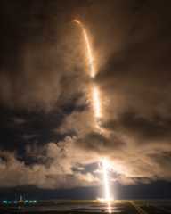 a white rocket lifts off at night above a plume of fire and smoke