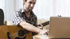 Man holding acoustic guitar in front of a silver laptop