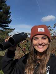 A woman holding solar binoculars and smiling during a partial solar eclipse.