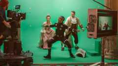 Directing green screen scene with gentleman protecting lady from actor playing monster wearing motion capture suit.