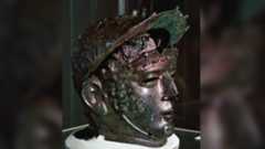 a greenish bronze helmet in the shape of a man's head and face