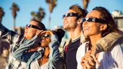 Four people wear solar eclipse glasses and look into the sky while smiling