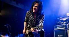 Steve Stevens wears a polka-dot shit and plays his Knaggs single-cut on a stage lit up in blue, Marshall stacks in the background.