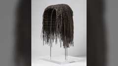 a wig made from dark-brown human hair rests on a stand against a white background
