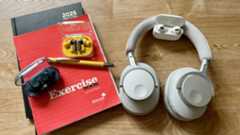 The Cambridge Audio Melomania P100, Sony WF-C710N, AirPods Pro 2 and Nothing Ear (a), which all feature in this student headphones guide, on a wooden table next to a stack of exercise books, a diary and a pen