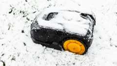 Robot lawn mower covered in snow on snow covered lawn