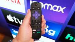 A Roku remote in hand in front of a TV with the Roku home page.