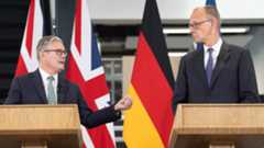 Keir starmer, left, and friedrich merz, right, look at eachother from behind podiums in front of union jack and german flags