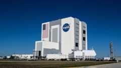 A white building with the American flag and NASA circle logo sits under a blue sky