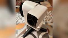 A white smart telescope with a black lens is standing on black legs on a tiled surface.