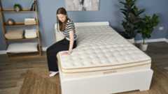A tester sits on the edge of the Saatva Classic mattress to test its support.