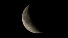 A close up of the moon in the darkness of space, with only a crescent shaped beam of light showing the surface