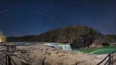 a lunar eclipse sequence arches overhead and a moonbow in the foreground in the mist of the nearby waterfall. 