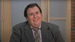 John Candy sits in an office with a worried smile in Uncle Buck.