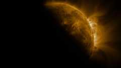 An image of the sun in space, with a dark shadow partially covering it where the moon crosses in front of it