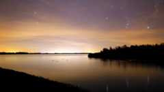 The constellation Orion is shown rising above a lake at sunset.