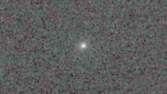 Comet 3I/ATLAS is feasible as a bright point of glowing light in the center of a pixelated black and dark grey background.