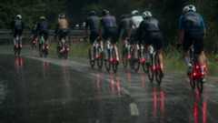 A group of cyclists cycling on a wet road in winter, each of them using a set of the best winter road bike tyres and with bright red lights on the rear of their bikes