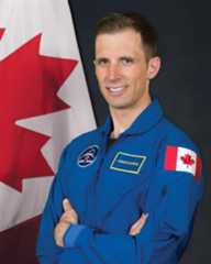 Canadian Space Agency astronaut Joshua Kutryk standing in front of a canadian flag with an astronaut suit on