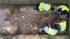 four people in blaze yellow vests excavate a trench full of human bones