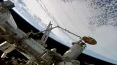 a spacecraft is held by a robot arm over Earth