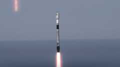A used black and white SpaceX rocket launches with the ocean horizon in the background.