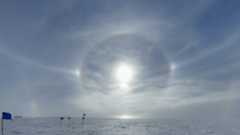 Rings of sunlight reflect against a snowy surface with a bright cloudy sky