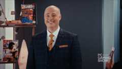 Sean Day9 Plott in a suit and tie with a shelf containing PC Gamer magazines behind him