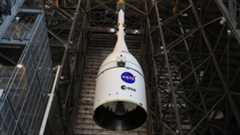 A white cone with NASA and ESA logos is lowered inside a large warehouse bay.