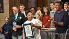 A group of people, including Gordon Ramsay and a Guinness World Records official, are smiling and laughing as a chef holds up a framed certificate.