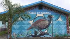 Photo of a the exterior of a building on which is a mural of a large bird as viewed from the side. Above the bird it says, "PAASAO LE MANUMEA."