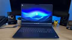 Alienware 16X Aurora gaming laptop open on a wooden desk with blue backlighting