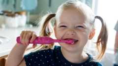 A little girl smiling while brushing her teeth with an electric toothbrush