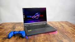 Asus ROG Strix G16 (G614FR) gaming laptop on a wooden desk against a gray background.