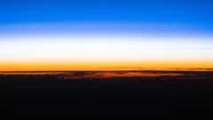 A sunset showing the black curve of the Earth with a golden band of light just above and a blue band of light above that