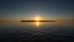 A sunset over a lake with a silhouette of an island right underneath the setting sun