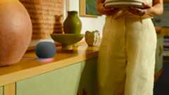 The Google Home Speaker in black, sitting on a countertop while a model walks by.