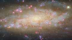 A glowing spiral galaxy is full of white, yellow and blue light with bursts of pink around the edges.